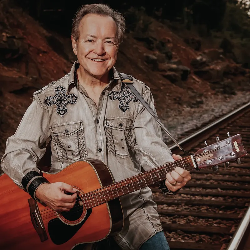 Bobby G. Rice strumming his guitar beside the tracks