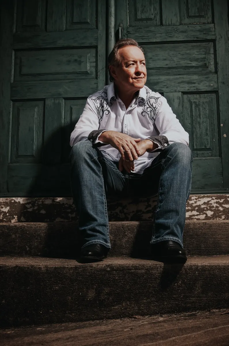 Bobby G. Rice seated on stone steps before a green door, wide shot