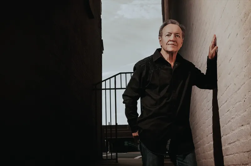Bobby G. Rice in black, one hand on a white brick wall