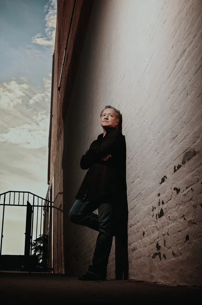 Bobby G. Rice leaning in a narrow brick alley under an evening sky