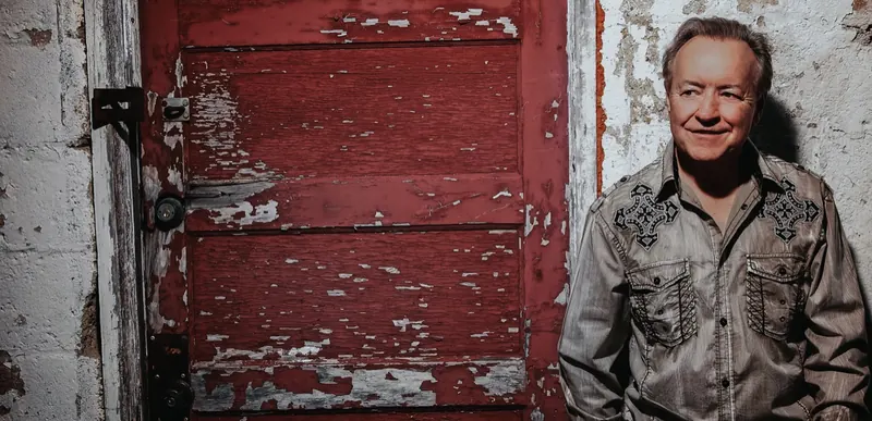 Bobby G. Rice smiling beside a weathered red door