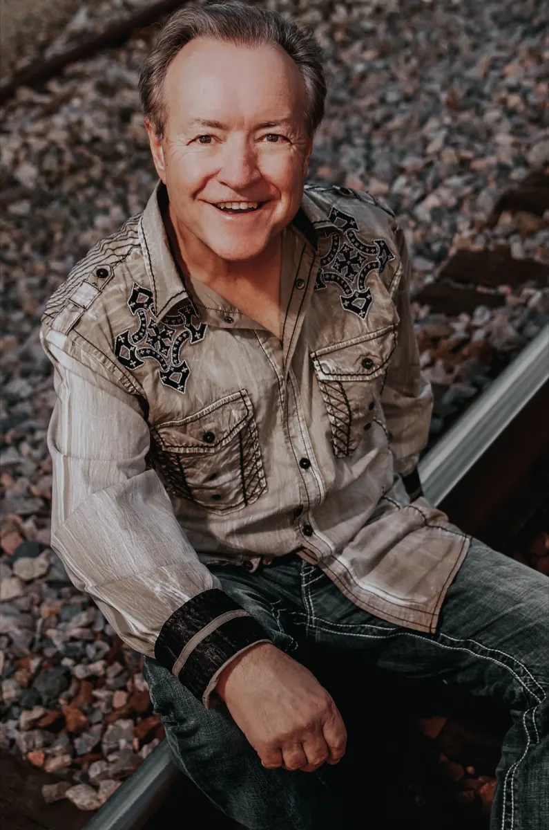 Bobby G. Rice sitting on a rail in an embroidered western shirt