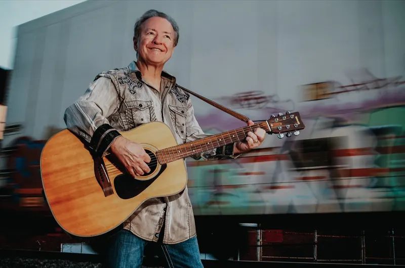 Bobby G. Rice playing guitar as a freight train rolls past
